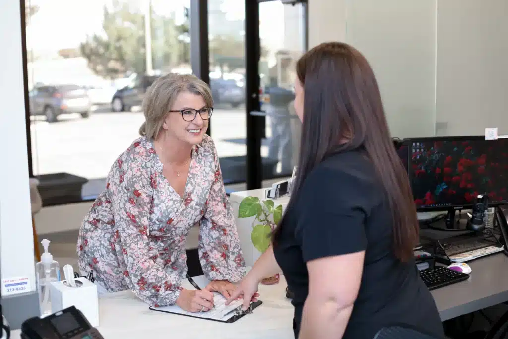 Front desk assistant at our Amarillo dental office talking to a patient as she is signing new patient forms.